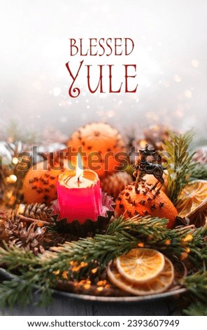 Blessed Yule greeting card. Winter altar for Yule sabbat. Candle, amulet deer, cones, decorated oranges and dry orange slices, fir branches on wooden table close up. Festive winter season.