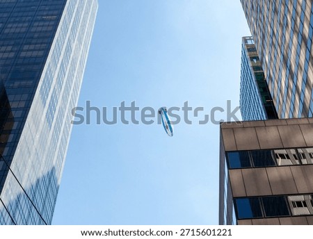 Blimp navigating a clear blue sky, capturing the contrast between a vintage form of advertising and the sleek, contemporary architecture of urban high rise buildings in the metropolitan skyline