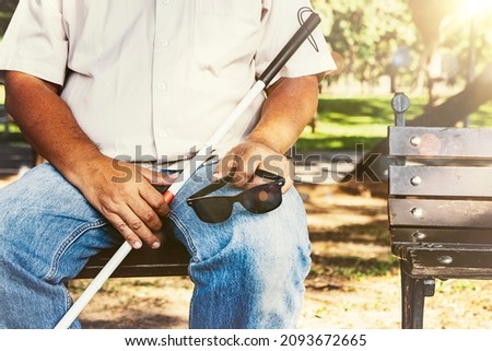 Blind asian pitiful senior elder brother sat calmly holding the blind stick and with his glasses removed, resting on his knees while exhausted on the bench.
