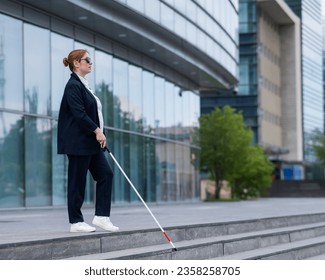 Blind business woman descending stairs with a tactile cane from a business center. - Powered by Shutterstock