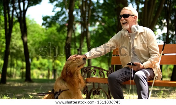 Blind man with earphones stroking dog, full life of\
impaired, enjoying time