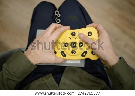 Blind man using tactile braille electronic device with large yellow buttons while sitting in library, hands holding assistive technology for visually impaired