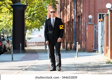 Blind Man Walking On Sidewalk Holding Stick Wearing Armband