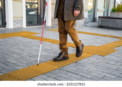Blind man with a walking stick. Walks on tactile tiles for self-orientation while moving through the streets of the city - Shutterstock ID 2231127815