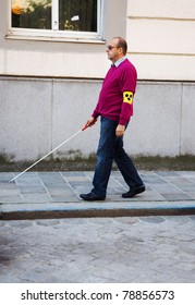 A Blind Man Walks With A Cane On A Street