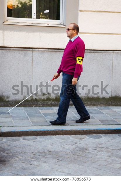 A blind man walks\
with a cane on a street