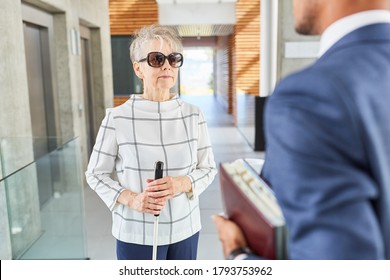 Blind old woman with cane in business office talks to a businessman