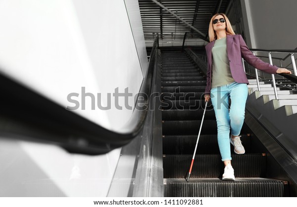 Blind person\
with long cane on escalator\
indoors