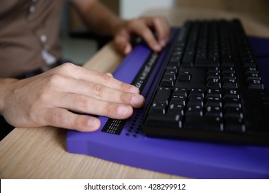 Blind person using computer with braille computer display and a computer keyboard. Blindness aid, visual impairment, independent life concept.