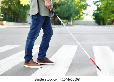 Blind person with white cane crossing street in city, closeup