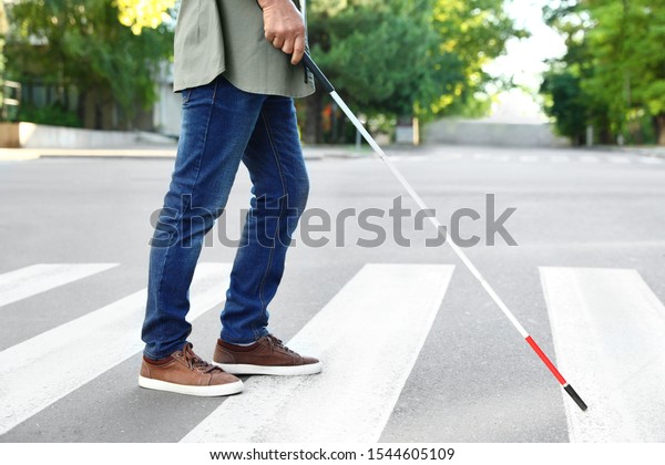 Blind person with white cane crossing street in\
city, closeup