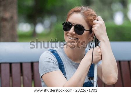 Blind red-haired woman sitting outdoors leaning on a cane. 