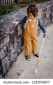 Blind Or Visually Impaired Child/Kid/Toddler/Preschooler/Boy Walking Through Neighborhood With Long White Cane, Exploring Concert Wall Ledge