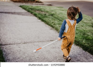 Blind Or Visually Impaired Child/Kid/Toddler/Preschooler/Boy Walking Through Neighborhood With Long White Cane; Back To Camera (Copy Space)