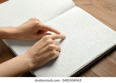 Blind woman reading book written in Braille at wooden table, closeup - Powered by Shutterstock