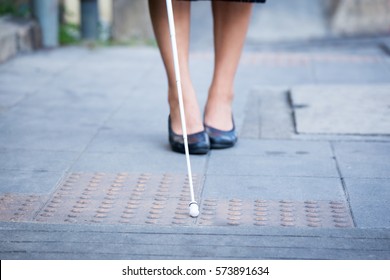 Blind Woman Is Walking On The Sidewalk, Using A White Cane.