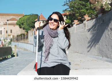 Blind woman with a white cane using a smartphone to listen some messages. Visually impaired concept with empty copy space.