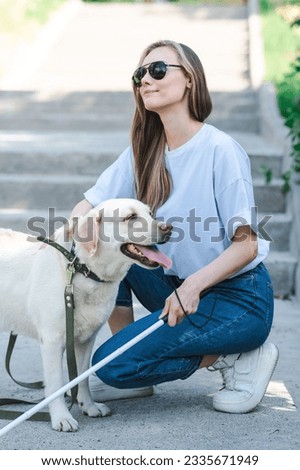 Blind young blonde petting a guide dog on a walk in the park. Woman with tactile cane at the stairs. 