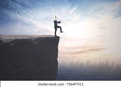 Blindfolded businessman with cardboard head finding a way and walks on the cliff with a city background