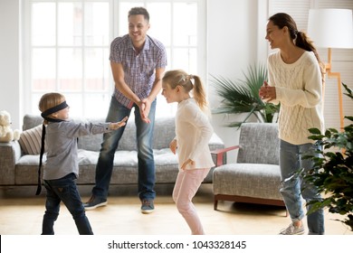 Blindfolded cute little boy playing hide and seek at home, parents and kids laughing spending time together enjoying game on weekend, happy family of four having fun leisure activity in living room