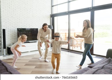 Blindfolded little boy playing hide and seek game at home, happy family of four having fun enjoying leisure activity in living room, parents and kids laughing spending free time together on weekend