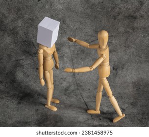 blindfolded wooden mannequin with white box on his head against dark background and his friend trying to help him - Powered by Shutterstock