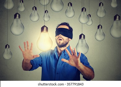 Blindfolded young man walking through light bulbs searching for bright idea 