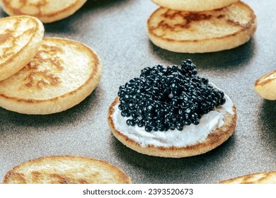 Blinis with black caviar and cream cheese, on a festive dish, mini pancakes, an elegant appetizer