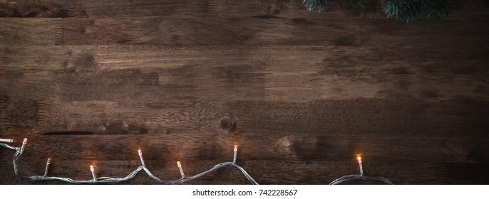 Blinking Christmas Decorative Light String With Green Pine Leaves On Wood Table Background, Top View Border Design Banner With Copy Space