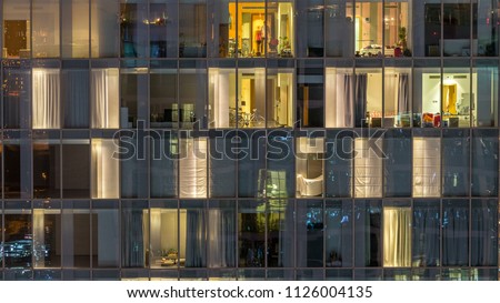Blinking and flashing windows of the multi-storey building of glass and steel lighting inside and moving people within timelapse. Aerial view of modern residential skyscrapers in Dubai downtown. Pan