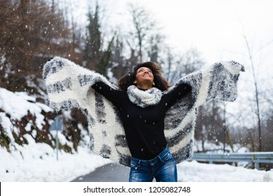 Blissful Black Woman Raising Arms Under The Snow In Winter At Mountain Road.