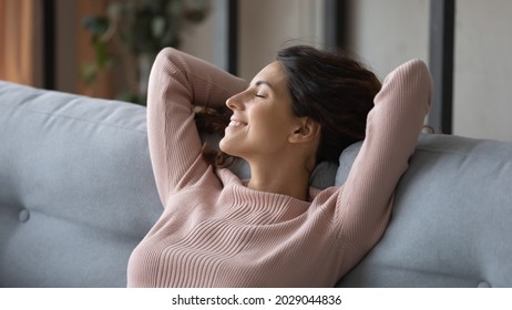 Blissful female closed eyes relaxing alone on comfy sofa at home, close up. Pretty young Latin woman put hands behind head breathing fresh conditioned air inside of modern house, stress-free concept - Shutterstock ID 2029044836