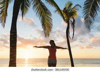 Blissful fitness woman enjoying outdoor summer sunrise or sunset workout at the beach. Happy female athlete exercising during vacation under tropical palms at Riviera Maya, Mexico.