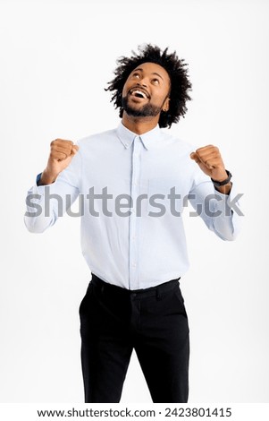 Blissful happy african-american male office employee raising clenched fists up in sign of victory, happy black man in formal wear celebrating success or good deal, looking up and thanking god
