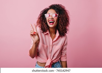 Blissful lovable woman with african hairstyle laughing during indoor photoshoot. Graceful cute girl in romantic casual clothes enjoying leisure time in studio.