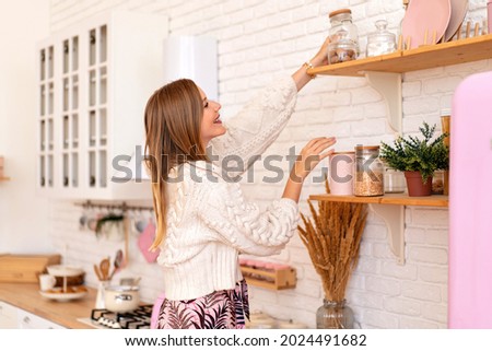 Blissful pretty blonde woman puts things and order and organizing stuff at her cozy kitchen, home style concept. 