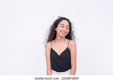 A blissful young asian with a beautiful smile closes her eyes while enjoying the moment. Isolated on a white backdrop. - Shutterstock ID 2243876829