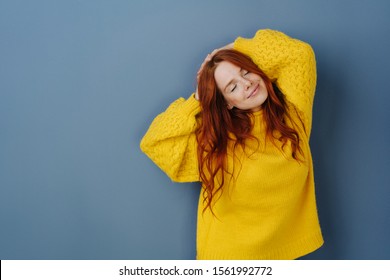 Blissful young woman enjoying a quiet moment to relax and de-stress standing with raised arms and closed eyes with a dreamy smile over a blue studio background with copy space - Shutterstock ID 1561992772
