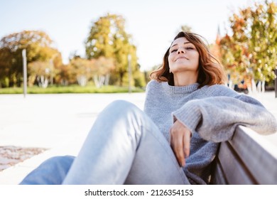 Blissful young woman relaxing on a bench in an urban park reclining back with her eyes closed and a serene expression in autumn - Shutterstock ID 2126354153
