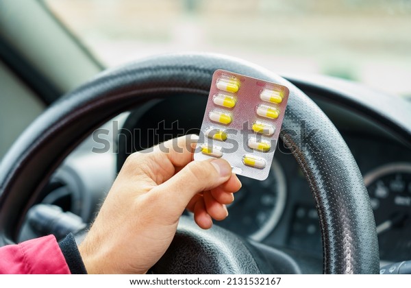 Blister\
of pills in the hands of the driver on a blurred background of the\
steering wheel in the car. The use of pharmacological drugs for\
medical purposes while driving. Selective\
focus