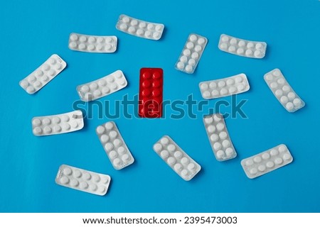 A blister of red tablets among scattered white tablets in blister packs on a blue background. Counterfeit drugs, needed medication, selection of necessary medications