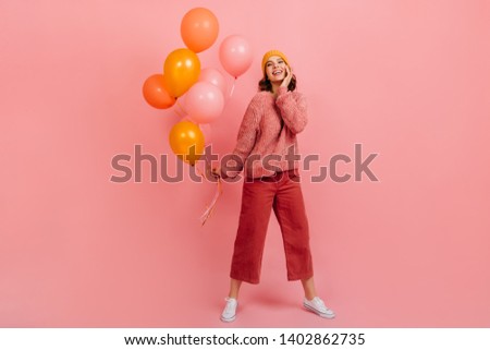Blithesome lady in hat dancing at party. Wonderful girl with air balloons posing on pink background.