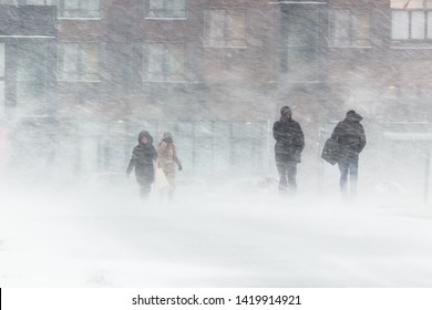 The blizzard, strong wind, sleet, against the background of houses blurred silhouettes of people, they try to hide from bad weather, overcome all difficulties of severe climate. go to the bus stop.