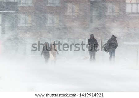 The blizzard, strong wind, sleet, against the background of houses blurred silhouettes of people, they try to hide from bad weather, overcome all difficulties of severe climate. go to the bus stop.