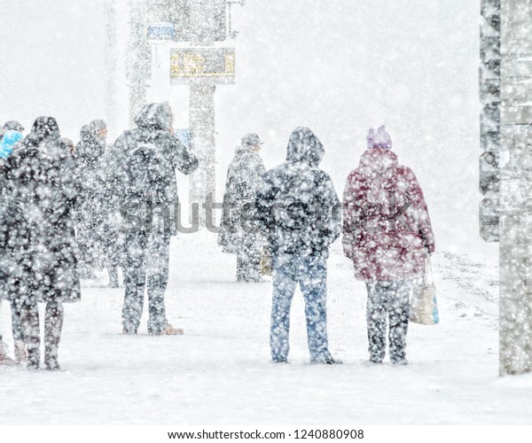 Blizzard in an urban\
environment. People on bus stop in snowfall. Abstract blurry winter\
weather background