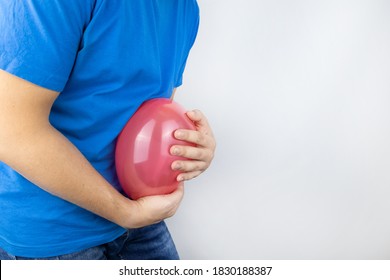 Bloating And Flatulence Concept. The Man Holds A Red Balloon Near The Abdomen, Which Symbolizes Gas Problems. Intestinal Tract And Digestive System