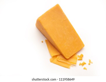 A Block Cheddar Cheese On Top Of Some Cheese Shavings And Crumbs On A White Isolated Background.