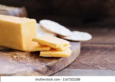 Block of cheddar cheese and slices over a rustic background.. Extreme shallow depth of field with selective focus on cheese. Water crackers in the background.   - Powered by Shutterstock