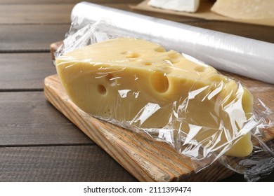 Block Of Cheese With Plastic Food Wrap On Wooden Table, Closeup