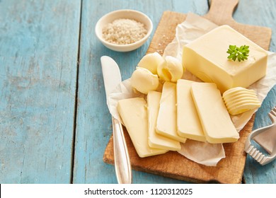 Bloque de mantequilla fresca cortada en tablero de madera contra mesa azul